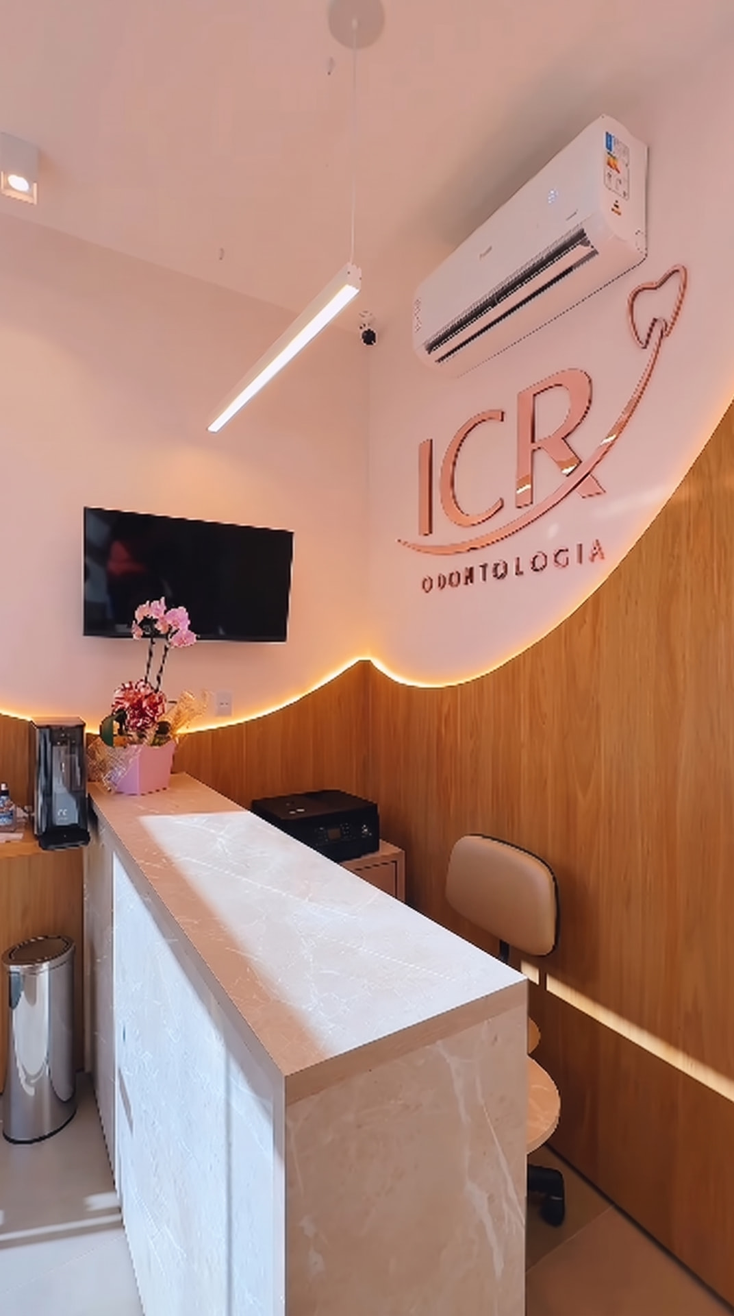 Recepção da ICR Odontologia com letreiro em rosé e painel de madeira clara